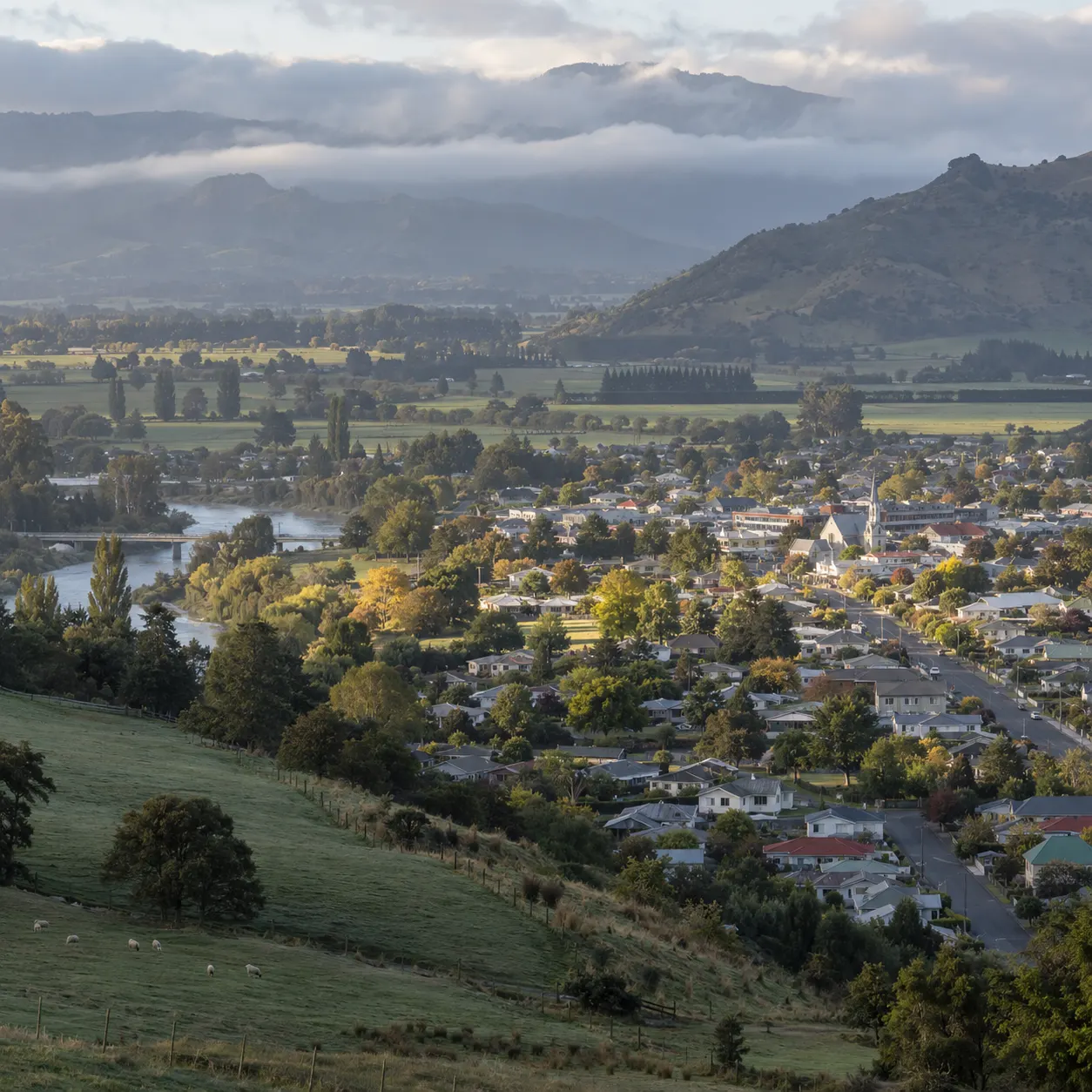 A New Zealand provincial town beside a river, with farmland and hills beyond